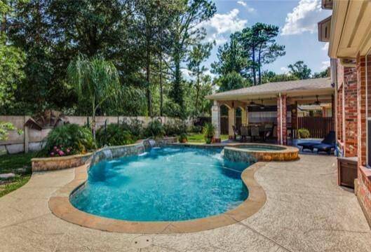 This photo showcases a luxurious backyard featuring a freeform pool with a waterfall feature. Adjacent is a covered patio with a kitchen and dining area, perfect for outdoor entertaining.