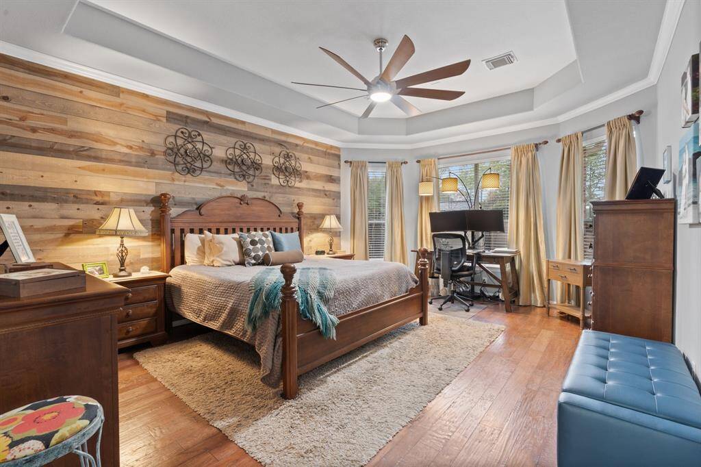 The spacious master bedroom features warm wood accents and a stylish ceiling fan. There is ample natural light from multiple windows.