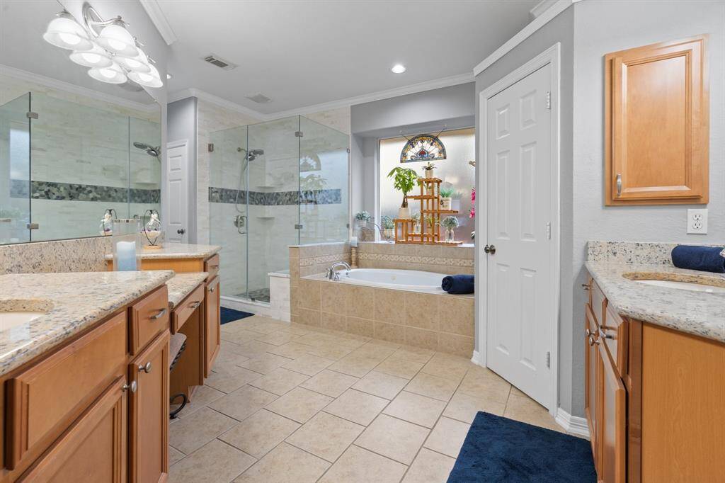 This bathroom features a spacious layout with dual sinks and granite countertops. It includes a large glass-enclosed shower and a separate jetted bathtub beneath a decorative window.