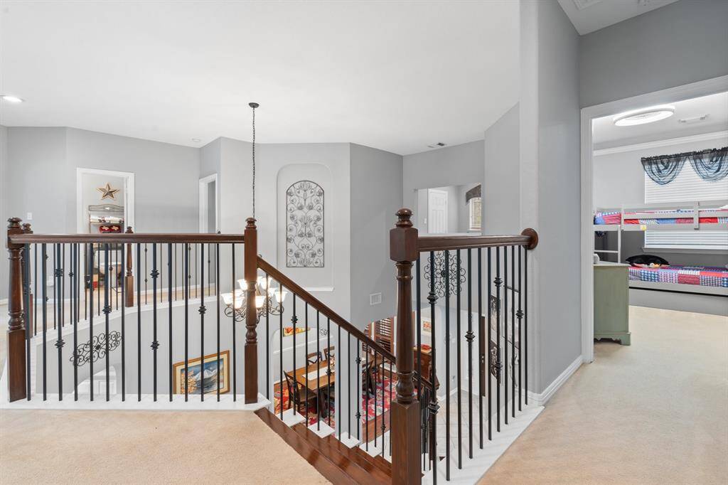 This photo shows an elegant upstairs landing with iron and wood railings, overlooking a spacious foyer.