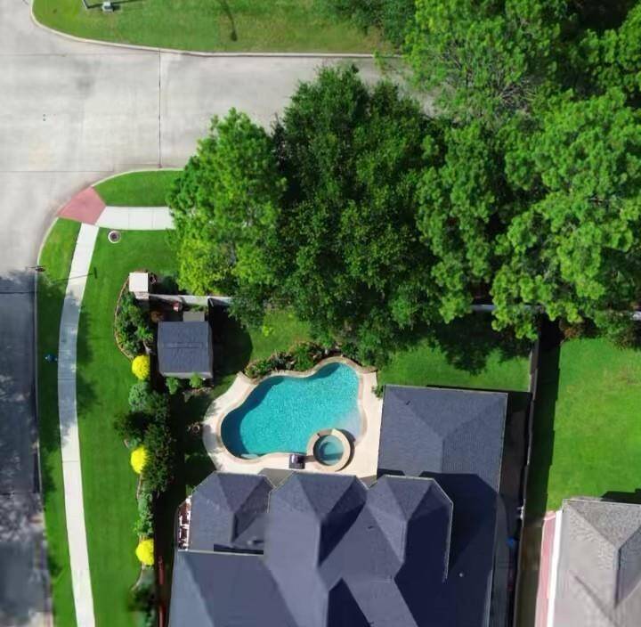 This aerial view showcases a beautiful home with a spacious backyard featuring a pool and spa. It is situated on a large corner lot in the community of Oakhurst.