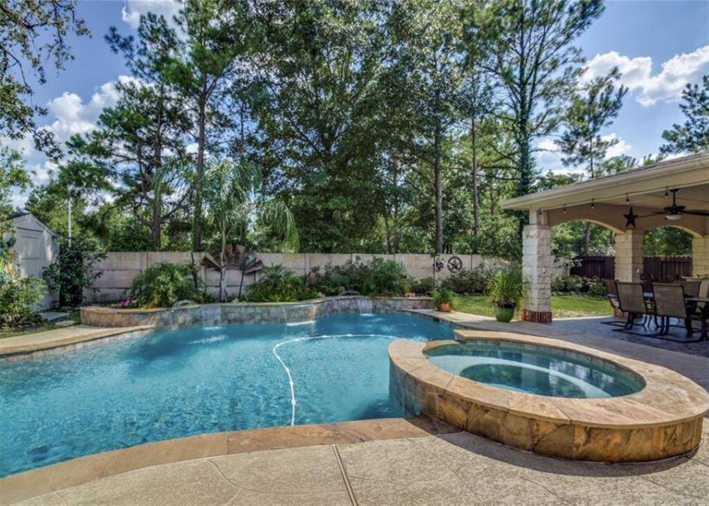 This backyard features a heated pool and waterfall with an attached hot tub. A covered patio with a ceiling fan offers a comfortable outdoor dining area.