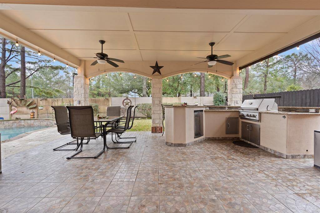 This outdoor space features a covered patio with ceiling fans, a tiled floor, and a built-in barbecue kitchen area for entertaining and relaxing.
