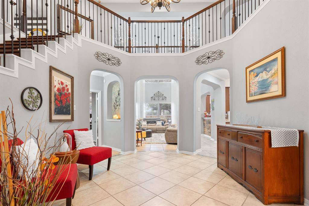 This welcoming foyer features high ceilings, elegant tile flooring, and a staircase with wrought iron railings. It leads into a spacious living area.