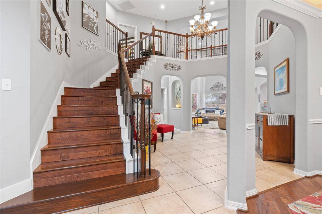This photo shows a spacious, elegant foyer with a wooden staircase and iron railings leading to an upper level. The layout includes arched entryways and a view into a cozy living area.