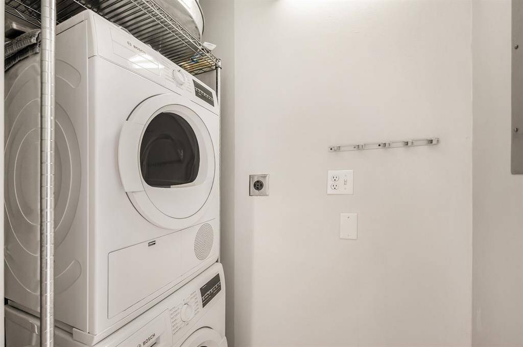 This is a compact laundry space featuring a stacked white washer and dryer set.  The area is clean and well-maintained with accessible power outlets and a wall-mounted clothes hanger.