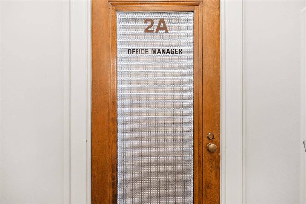 This is a photo of the entrance wooden door with glass paneling, labeled "2A" and "OFFICE MANAGER." The glass provides some level of privacy while still allowing light to filter through.