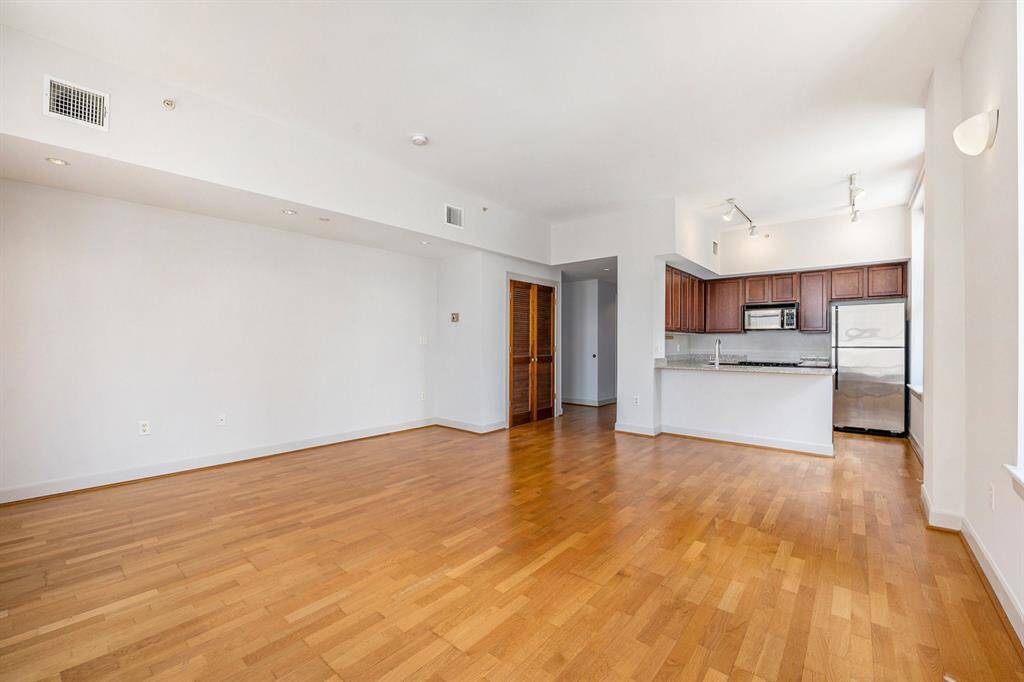 This is a bright, open-concept living space featuring hardwood floors, a modern kitchen with stainless steel appliances, and ample wall space for customization.