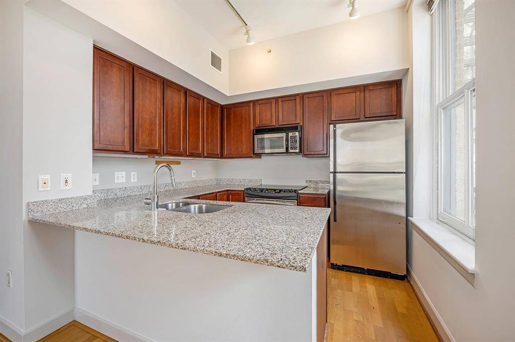 This is a modern kitchen featuring hardwood floors, granite countertops, stainless steel appliances, and cherry cabinets, complemented by ample natural light from a large window.