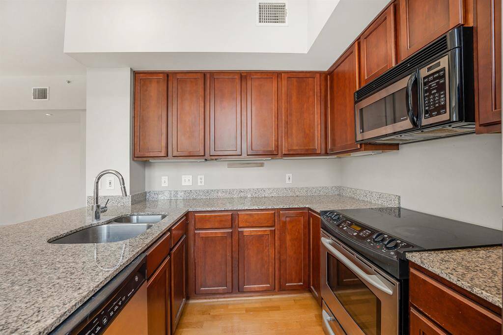 This is a modern kitchen with rich cabinetry and granite countertops, featuring stainless steel appliances and a built-in microwave.