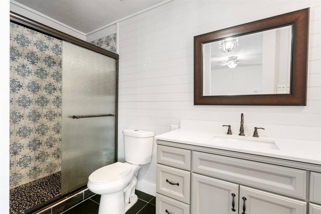 Updated bathroom features a stylish walk-in shower with patterned tiles and a frosted glass door. It includes a modern vanity with a sleek sink, a large framed mirror, and a classic white toilet. The space is bright and contemporary.