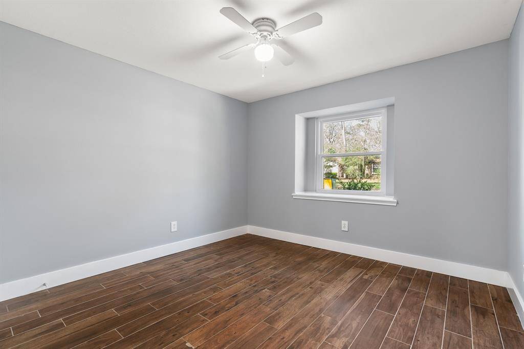 Second bedroom features light gray walls, rich wood-look tile flooring, and a central ceiling fan. A large window offers plenty of natural light and a view of the outdoors, creating a cozy and inviting space.
