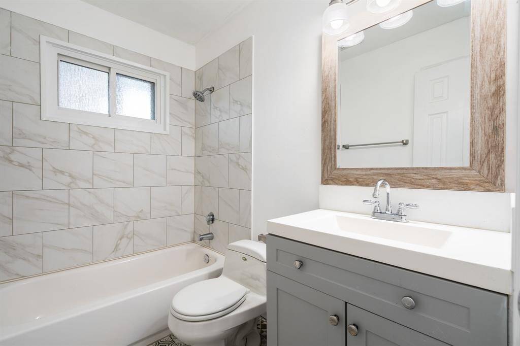 Secondary bathroom features a modern design with a white bathtub and toilet, elegant marble-patterned tiles, a sleek vanity with a wood-framed mirror, and stylish lighting.