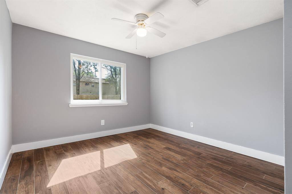 Bright and airy room bedroom featuring gray walls, a large window with natural light, a ceiling fan, and rich tile flooring. Perfect for a bedroom or office space.