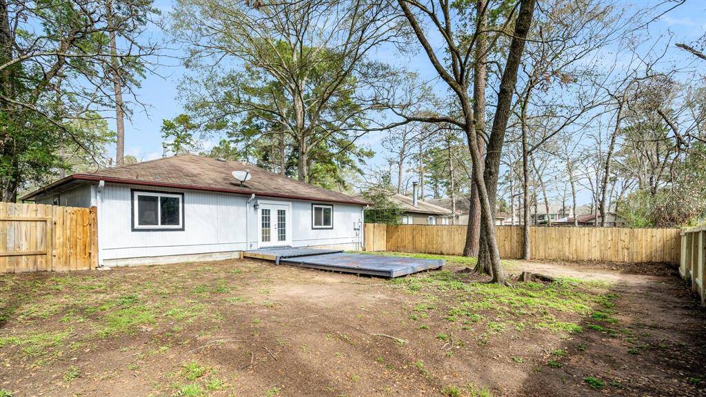 Backyard featuring a modest single-story home with a light exterior. The yard is spacious with mature trees and a wooden deck, perfect for outdoor activities. The area is enclosed by a wooden fence, providing privacy.