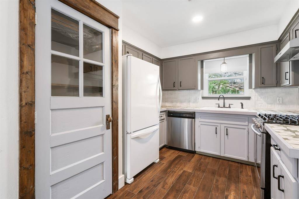 Charming kitchen with a rustic touch, featuring tile floors, gray cabinetry, and a farmhouse-style pantry door. Includes modern appliances, a window above the sink, and ample counter space.
