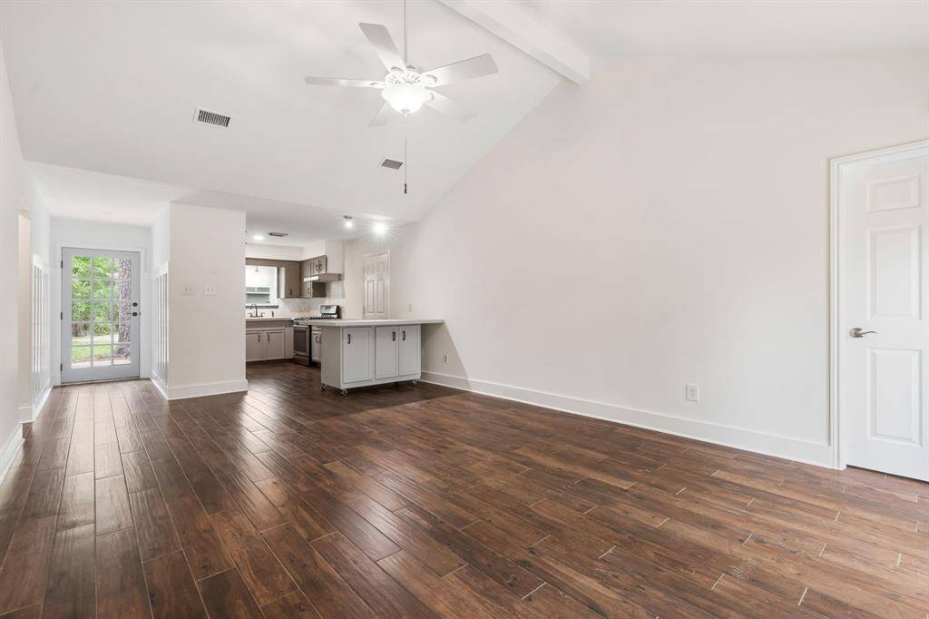 Bright open-concept living area with high ceilings, tile flooring, and a modern ceiling fan. The space flows into a contemporary kitchen with shaker style cabinetry and stainless steel range. White refrigerator is included with the home.  A door leads to an outdoor area, providing natural light and access to the backyard.