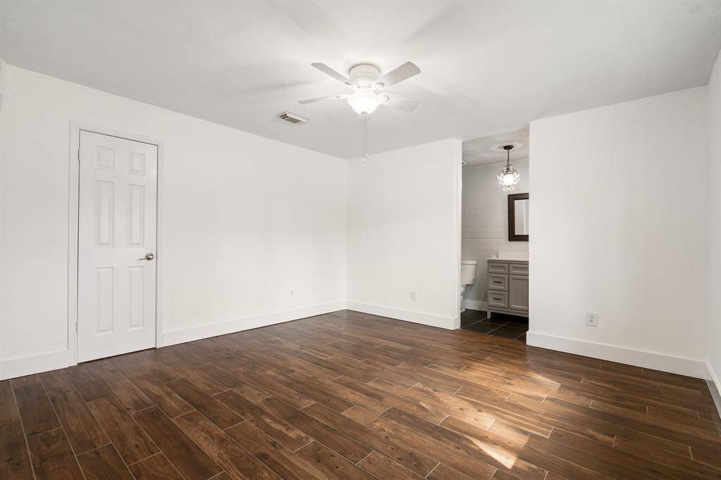 Primary bedroom with tile flooring, neutral walls, and a ceiling fan.  Adjoining bathroom featuring a vanity, walk-in shower and updated lighting.