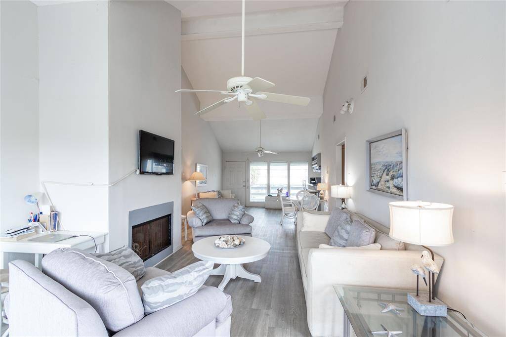 This spacious living room features high ceilings and neutral tones, creating a bright and airy atmosphere. It includes comfortable seating, a mounted TV, and a fireplace (not working), with large windows providing natural light. Perfect for relaxation and entertaining.