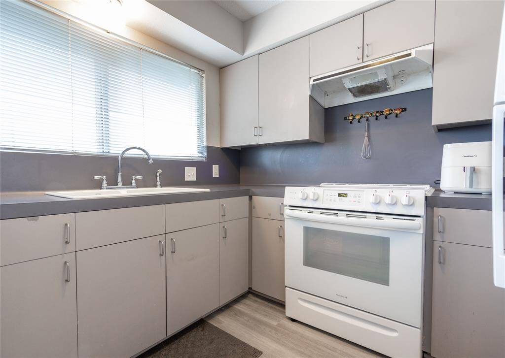 Modern kitchen with sleek grey cabinets, a white stove, and ample counter space. The large window provides plenty of natural light, enhancing the clean and functional design.  New kitchen sink and faucet.