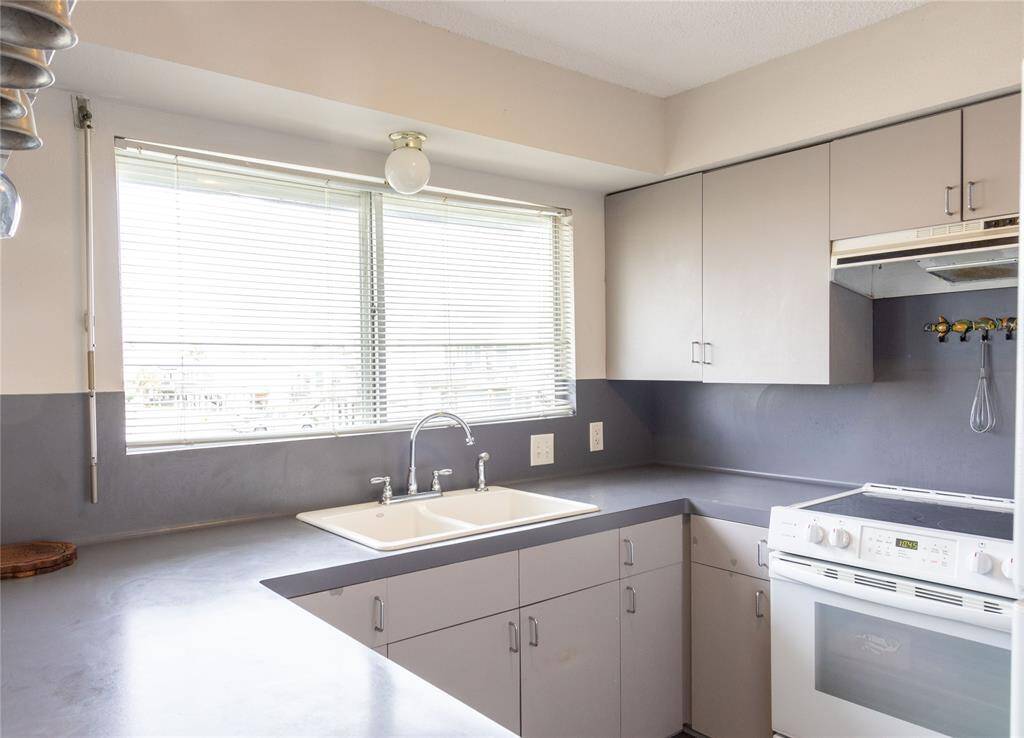 Bright kitchen with modern gray cabinetry, white appliances, and ample counter space. Large window provides natural light, enhancing the clean and functional design.