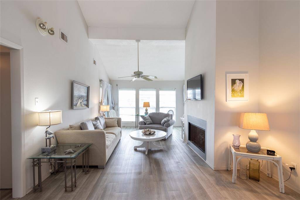 This photo showcases a bright, open living room with high ceilings and large windows that let in plenty of natural light. The space features modern furnishings, a cozy fireplace (seller does not use), and light vinyl plank flooring, creating a warm and inviting atmosphere.