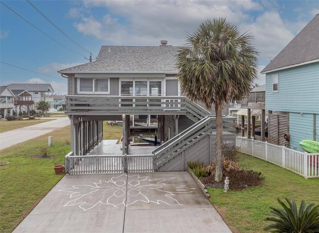 This coastal/canal home on a corner lot features a spacious front deck, covered parking, and a charming driveway with hand painted floral design. A mature palm tree adds to the tropical feel, and the house is situated in a friendly neighborhood, ideal for enjoying beachside living.