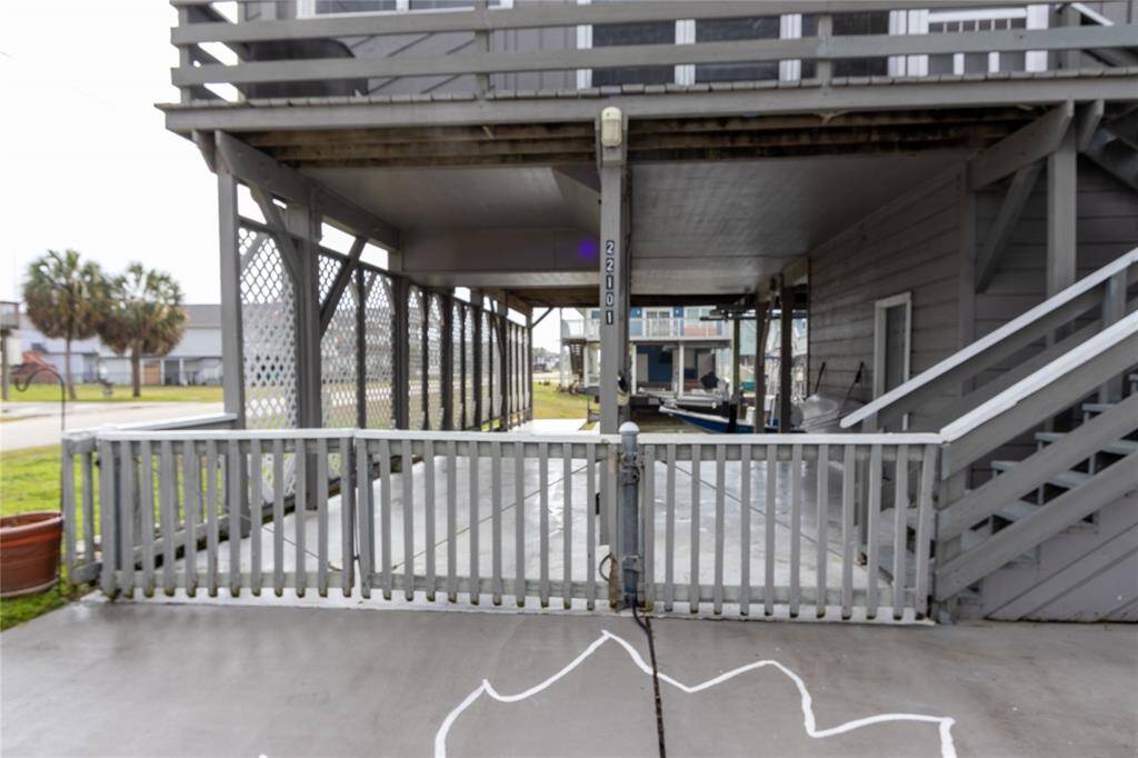 This photo shows an elevated home with a covered parking area below. The structure features a staircase leading to the main entrance, and a lattice design for added privacy and style. It's located in a neighborhood setting with visible green space and neighboring homes.