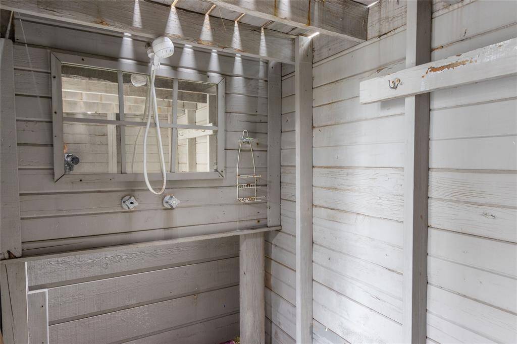 This photo shows an outdoor shower area with wooden paneling and a simple showerhead. Natural light filters through gaps above, creating a cozy, natural ambiance.