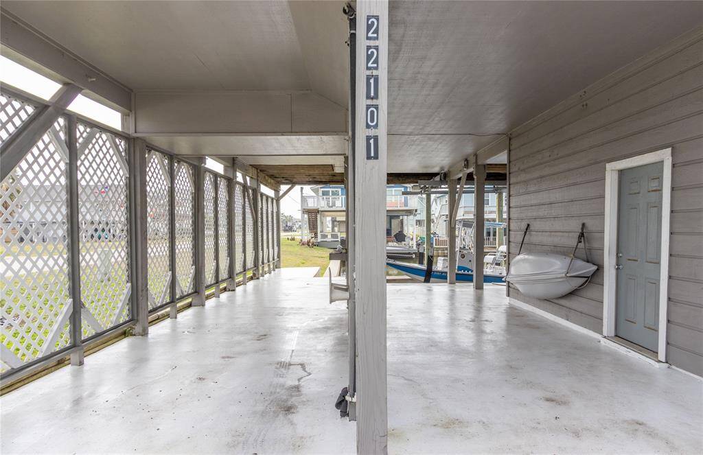 This photo showcases a spacious covered patio area with white flooring and lattice fencing. It features a side door to the large stiorage area and room for boat storage/RV storage, offering a view towards a canal and nearby houses, ideal for outdoor relaxation and storage.