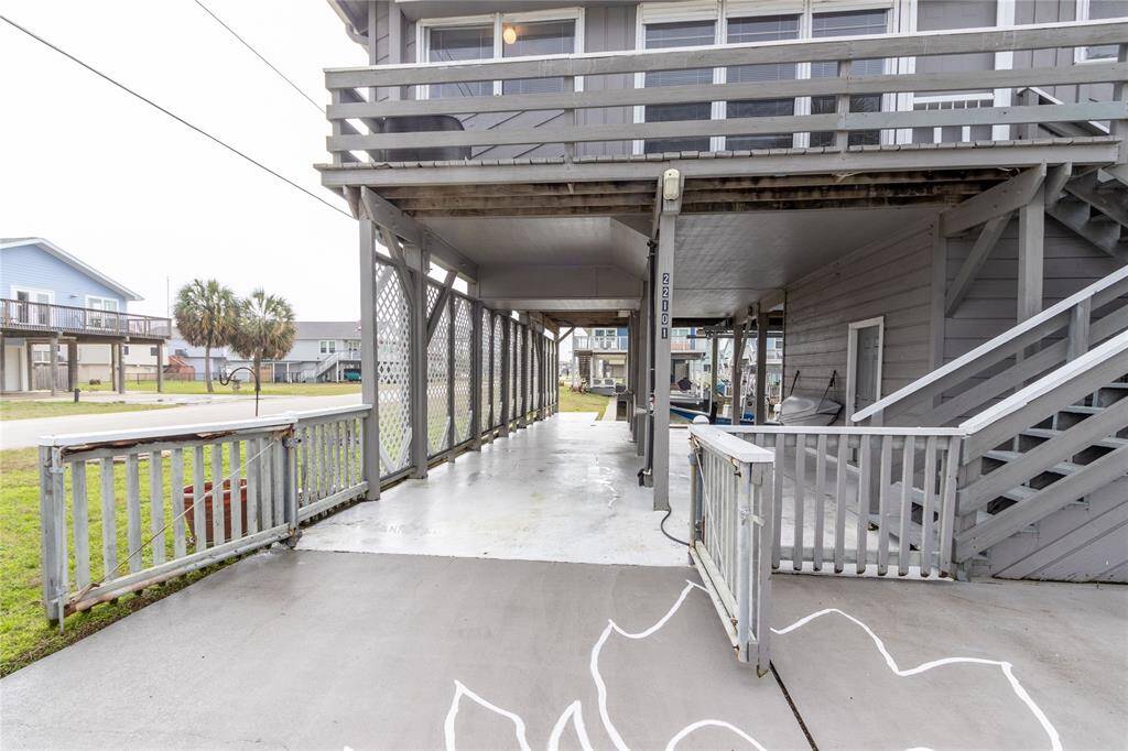 This photo shows a raised coastal canal-style home with an open ground-level area, for parking or outdoor activities. There are stairs leading to the main entrance, and the exterior features gray hardi plank siding