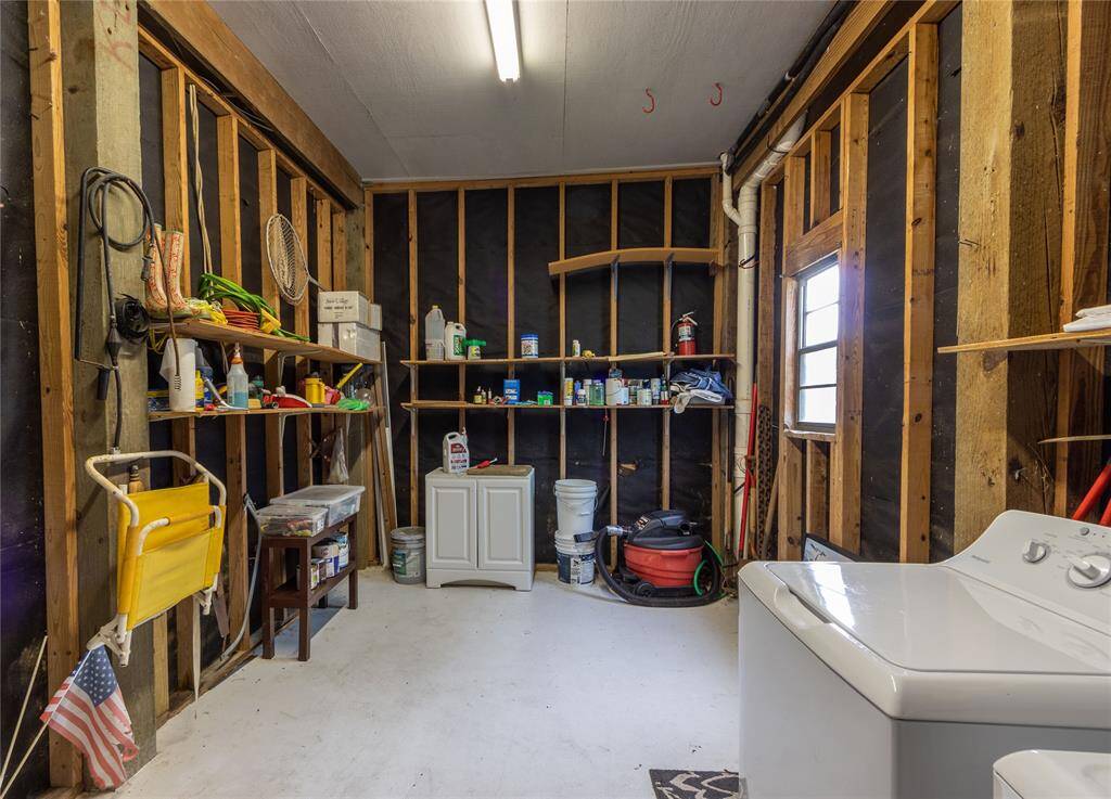 This photo shows a utility room with exposed wooden walls and ample shelving for storage. It includes a washing machine/dryer and various cleaning supplies, providing a functional space for laundry and organization.