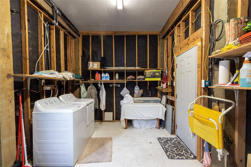This photo shows a utility room with exposed wooden framing and insulation. It features a washer and dryer, shelving for storage, and a utility sink. The space is practical for laundry and storage needs.