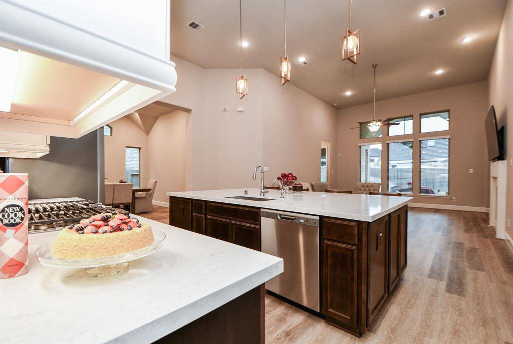 This open-concept kitchen and living area features high ceilings, modern pendant lighting, and large windows for natural light. The kitchen boasts a spacious island with a sink, stainless steel appliances, and sleek quartz countertops, ideal for entertaining and family gatherings.