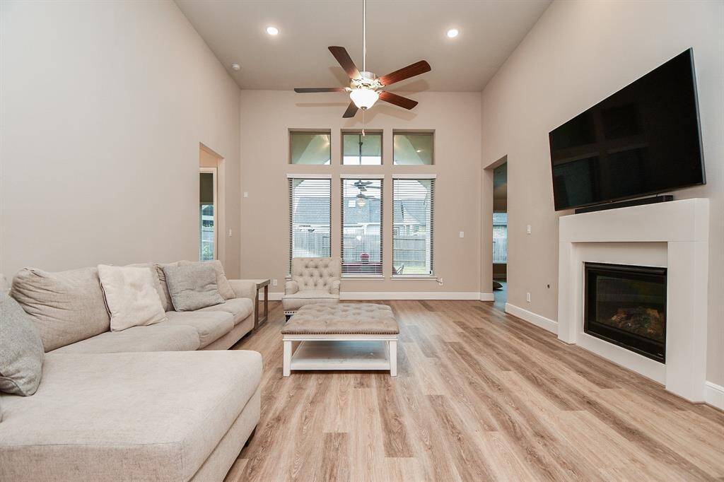 This spacious living room features high ceilings, a ceiling fan, and large windows that provide plenty of natural light. It includes an upgraded fireplace, creating a warm and inviting atmosphere.