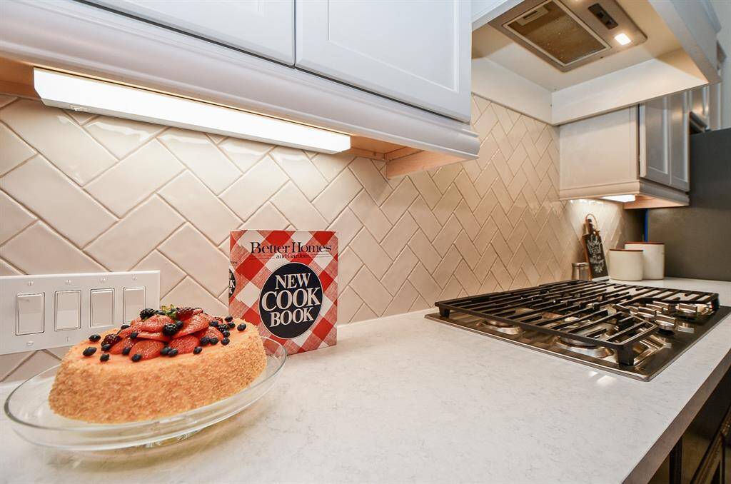 This modern kitchen features a sleek gas stovetop, elegant herringbone backsplash, and under-cabinet lighting. The countertop space is perfect for cooking and gatherings.