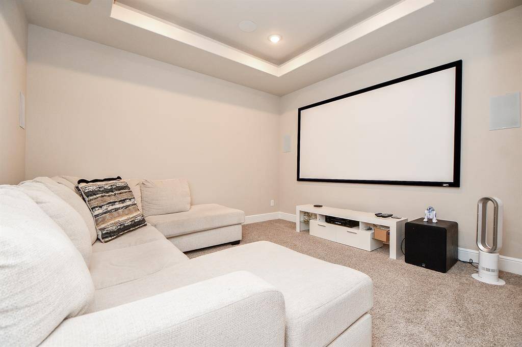 Cozy home theater room featuring a large screen, comfortable sectional sofa, and soft carpet flooring. Perfect for movie nights or entertaining guests.