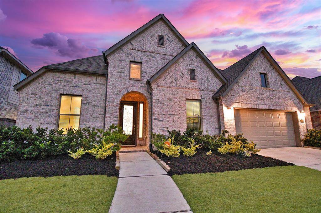This charming home features a classic brick exterior and a welcoming arched entryway. It is complemented by a well-maintained lawn and landscaped shrubs.
