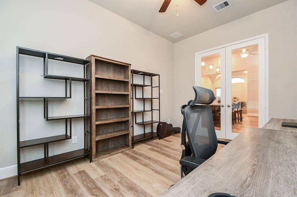 This spacious home office features a ceiling fan, modern shelving, and French doors leading to the kitchen and family room.