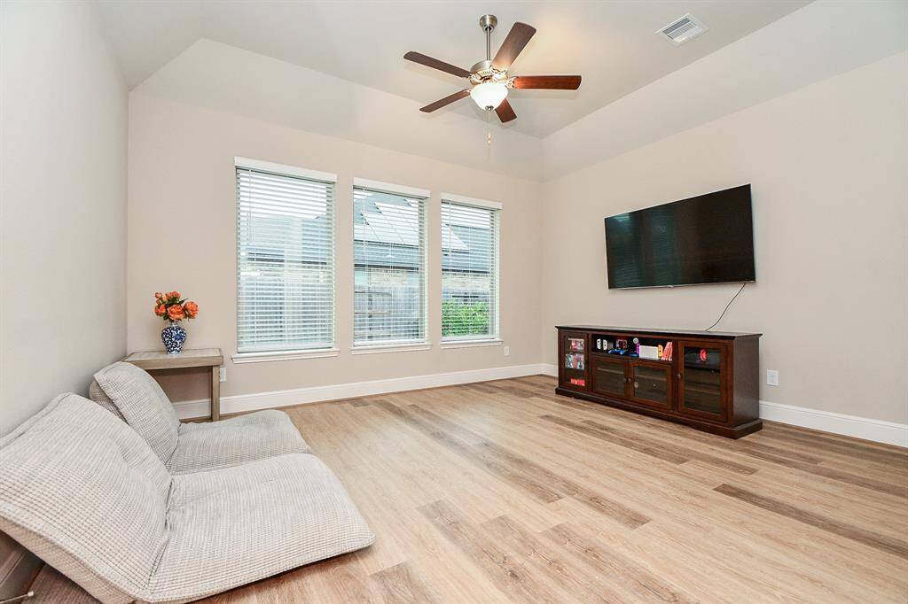 Bright and spacious game room featuring large windows, high ceiling with a ceiling fan, and space for entertainment setup.