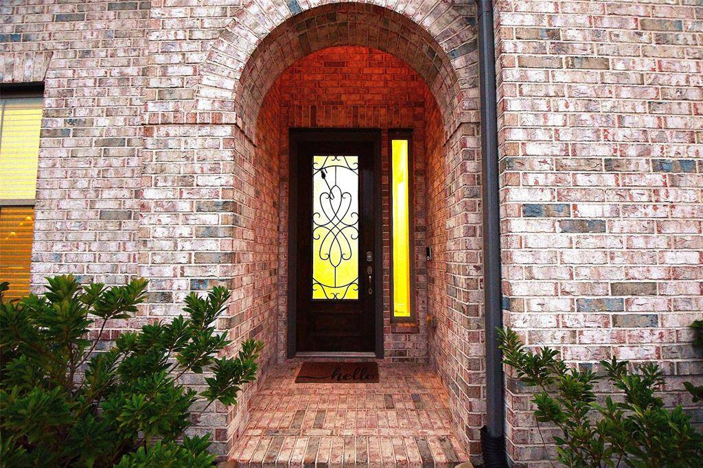 This showcases a charming brick entryway with an arched design and the front door features a wood door with decorative wrought iron and glass panel.