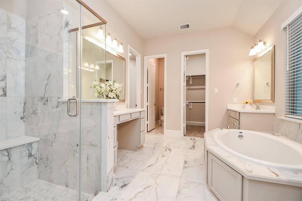 Elegant primary bathroom showcases a large glass-enclosed shower, a luxurious soaking tub, and dual vanities and a makeup vanity with ample storage.