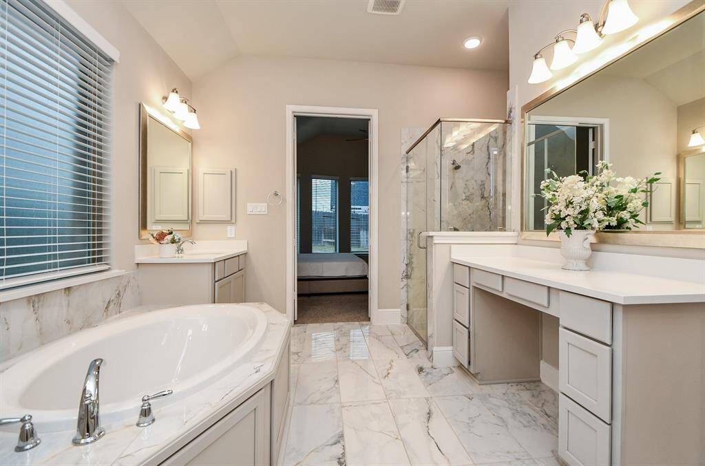 This spacious bathroom features a luxurious soaking tub, a glass-enclosed shower, and three  vanities with ample storage. The elegant tile flooring and soft lighting create a serene atmosphere.