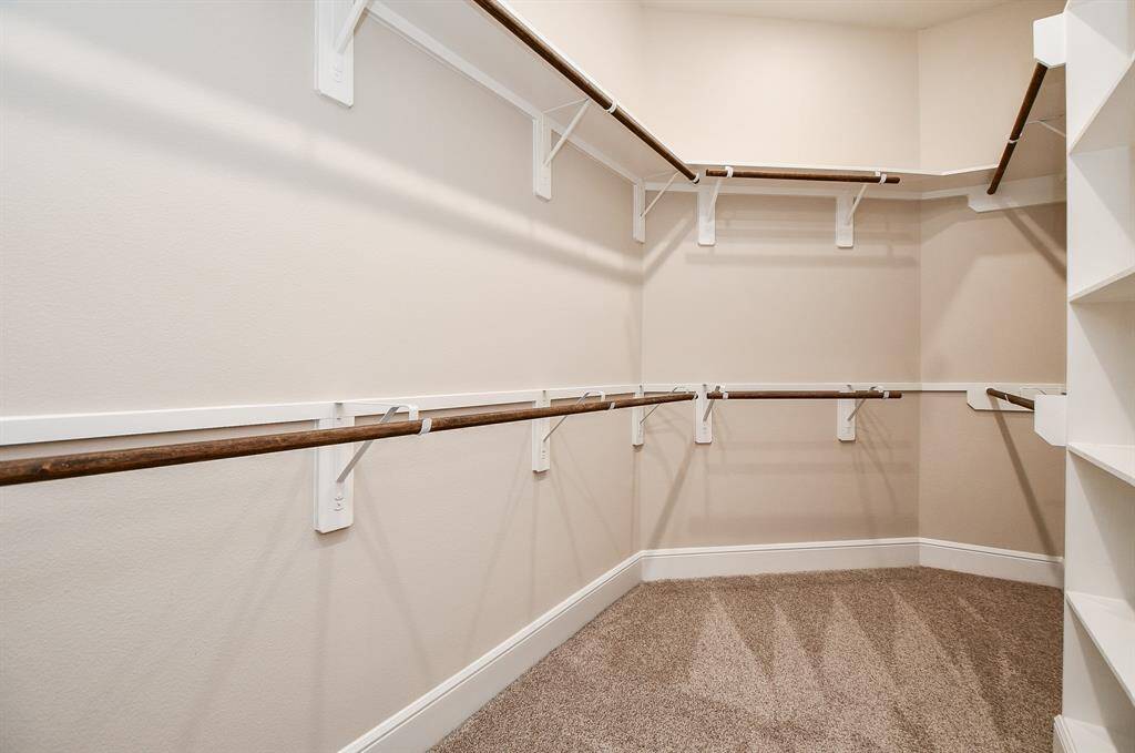 Primary bathroom has a spacious walk-in closet with, carpeted flooring, and multiple wooden rods for hanging clothes. It also features shelving for additional storage.