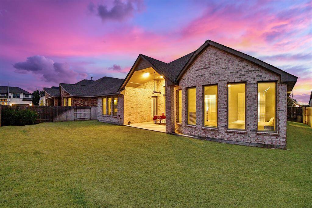 This photo showcases a modern brick home with a spacious backyard, large windows, and a covered patio.
