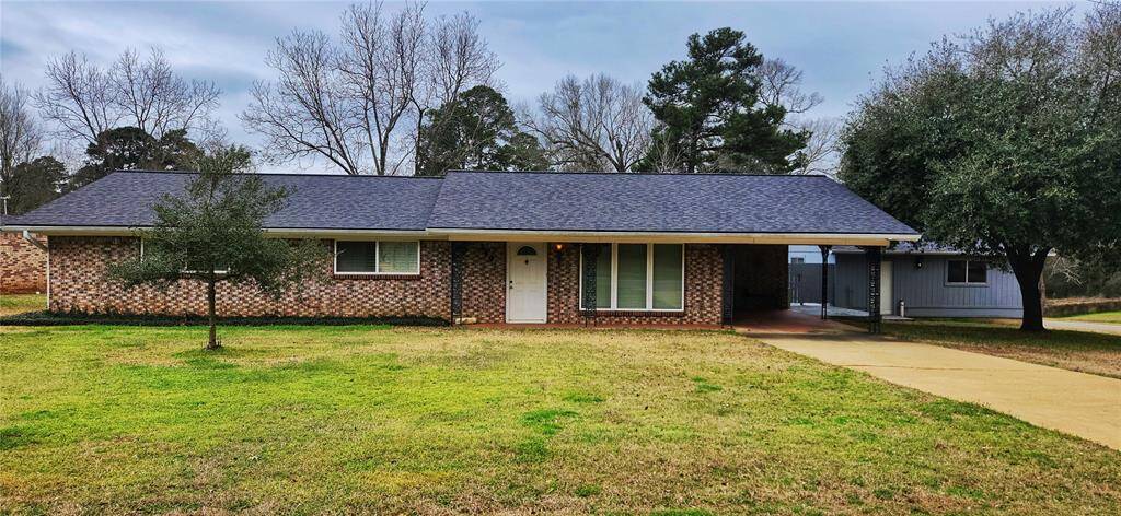 This charming single-story home features a classic brick exterior with a neatly maintained front lawn and mature trees. A covered carport provides convenient parking, and large windows offer plenty of natural light. The setting is peaceful, with a spacious yard perfect for outdoor activities.