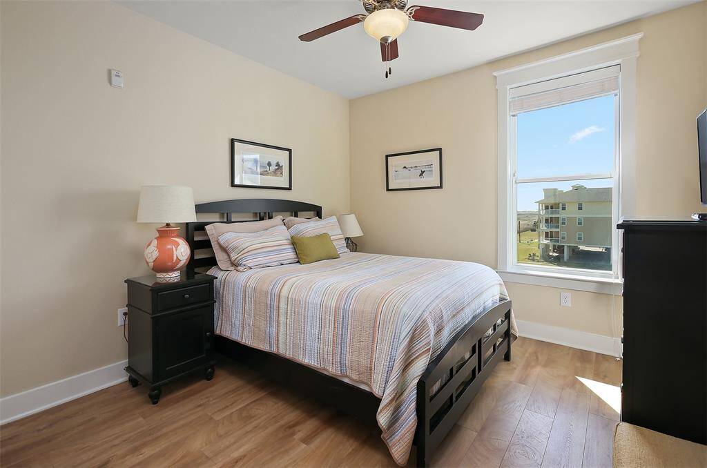 This bright and airy second bedroom features a large window with Gulf views, a ceiling fan for added comfort, and a soothing coastal color palette.