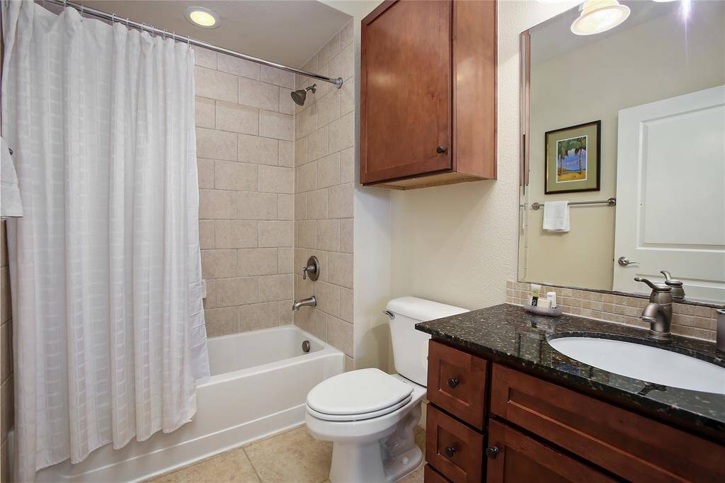 The second bathroom boasts a granite vanity, tiled shower/tub combo, and warm wood cabinetry, offering both style and convenience.
