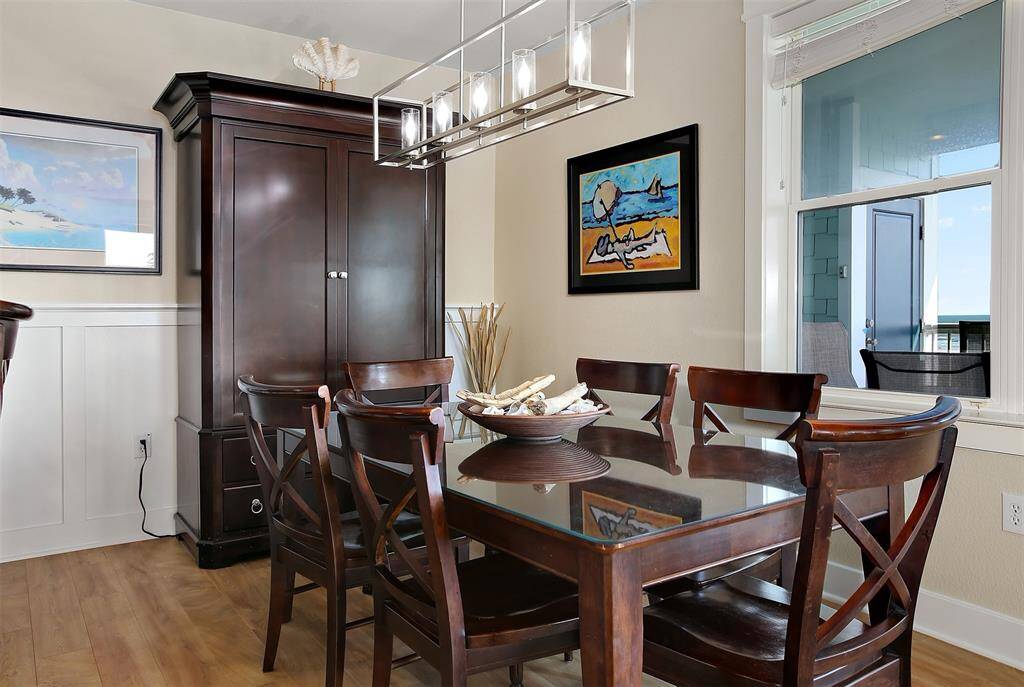 Gather around this elegant dining space, featuring a sleek glass-top table, rich wood finishes, modern lighting, and a window view of the Gulf.