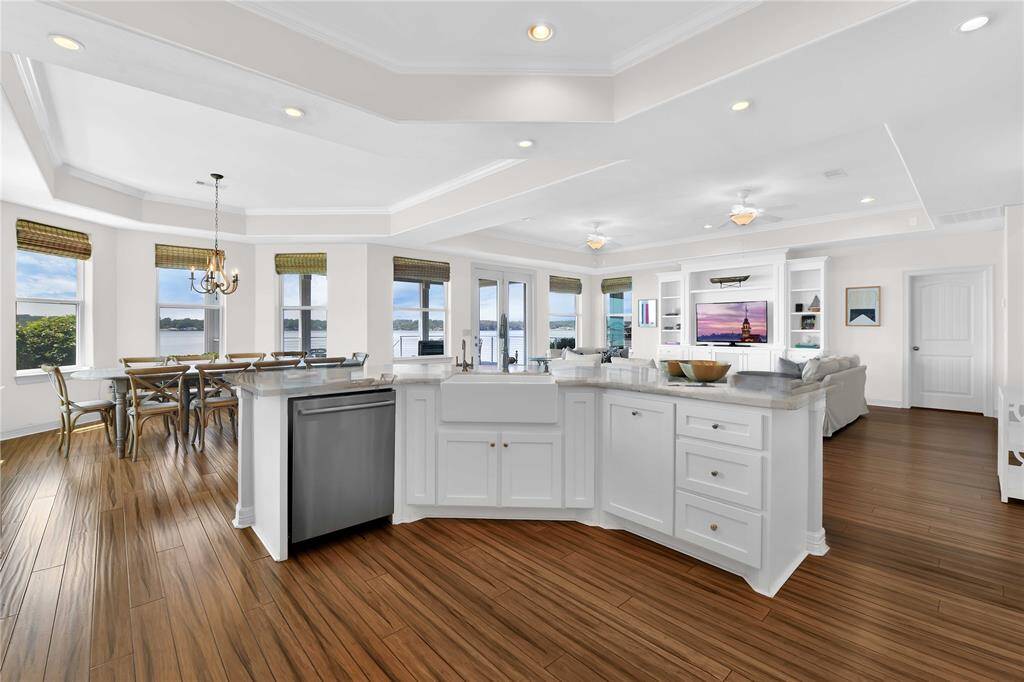 This open-concept living space features a modern kitchen with an island, elegant hardwood floors, and ample natural light from multiple windows offering scenic water views. The adjacent dining and living areas are spacious and airy, perfect for entertaining.